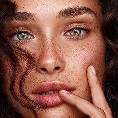 a woman with freckles on her face and hands near her face, looking at the camera