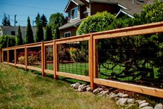 a wood and wire fence in front of a house with green grass on the side