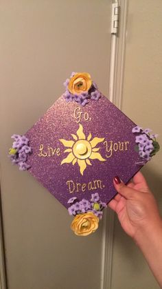 someone holding up a purple graduation cap that says go live your dream with flowers on it