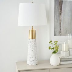 a table with a lamp, vase and flowers on it next to a painting in the background