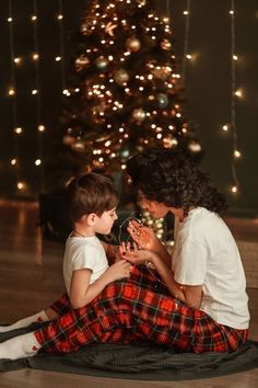 a mother and son sitting on the floor in front of a christmas tree looking at each other