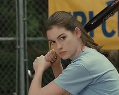 a young woman holding a baseball bat in her right hand and looking at the camera