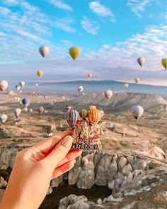 a person holding up a small card with hot air balloons flying in the sky above