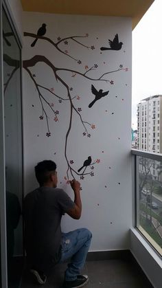 a man is painting a tree with birds on the branch and flowers on the wall