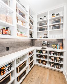 a kitchen with white cabinets and shelves filled with food items on the counter top, along with wooden flooring