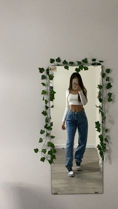 a woman taking a selfie in front of a mirror with ivy growing on it