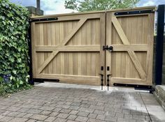 a large wooden gate with black hardware on the top and bottom bars, in front of a brick walkway