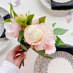 a person holding a bouquet of flowers in front of plates and silverware on a table