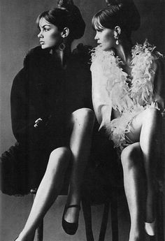 two women sitting next to each other in high heeled shoes and fur stolers