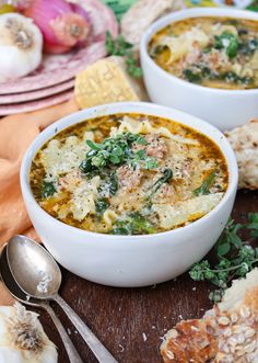 two white bowls filled with soup on top of a wooden table next to garlic bread