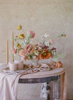 an arrangement of flowers and candles on a table with a cloth draped over the table