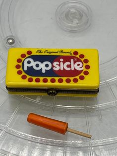 a yellow pop slice box sitting on top of a clear plastic tray next to an orange stick