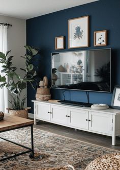 a living room with blue walls and a white entertainment center in the foreground is a large potted plant