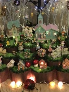 a table topped with lots of fake grass covered in little fairy houses and lights next to candles