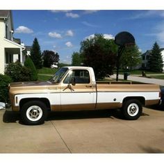 a brown and white truck parked in front of a house next to a black car