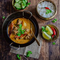 two bowls filled with food on top of a wooden table next to rice and cucumbers