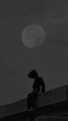 a man sitting on top of a cement wall under a full moon