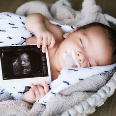 a baby laying in a blanket holding an electronic device