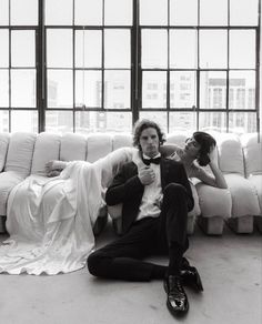 a man and woman laying on the floor in front of a white couch with large windows