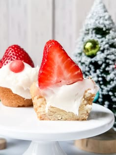 two cupcakes with white frosting and strawberries are on a cake plate