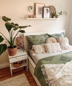 a bed with green and white sheets, pillows and blankets on it next to a potted plant