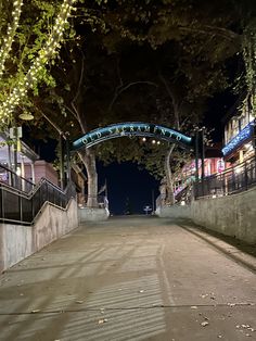 an empty street at night with lights on the trees and buildings in the background,