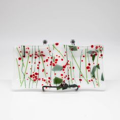 a glass plate with red flowers and green leaves on it, sitting on a white surface