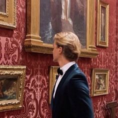 a man in a tuxedo looking at paintings on the wall