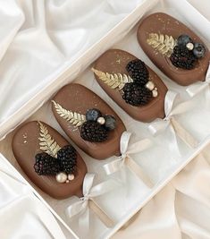 four chocolates decorated with berries and leaves in a box