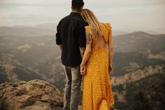 a man and woman standing on top of a mountain looking out at the valley below