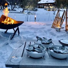 a fire pit with oysters and wine glasses in the snow