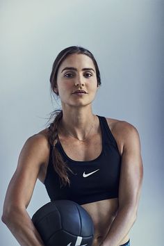 a woman holding a ball in her right hand and wearing a black sports bra top