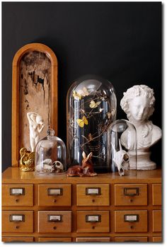 an antique dresser with glass domes and statues on it's top, in front of a black wall