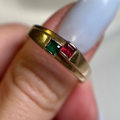 a woman's hand holding a gold ring with two emerald and red stones on it