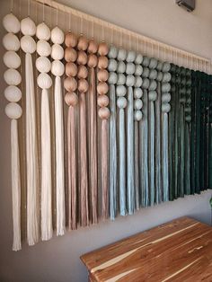 a wooden table sitting in front of a wall hanging with balls and tassels