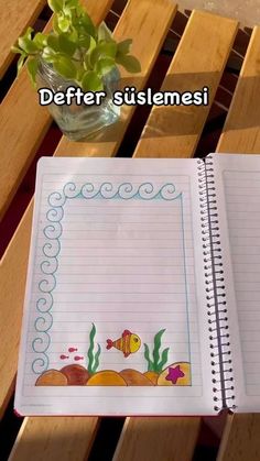 an open notebook sitting on top of a wooden table next to a vase filled with flowers