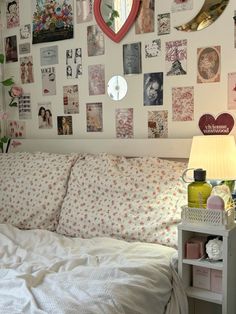 a white bed topped with lots of pillows next to a wall covered in pictures and heart shaped mirrors