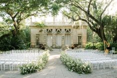 an outdoor ceremony set up with white chairs and greenery in front of a building