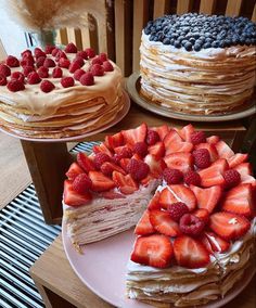 three different types of cakes with strawberries and blueberries on each cake plate, one has a slice missing