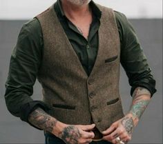 a man with tattoos on his arm wearing a brown vest and green shirt is looking at the camera