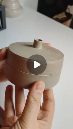 a person is holding a clay container in their hand with the lid open and there is a video playing on it