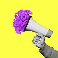 a person holding a megaphone with purple flowers on it's head in front of a yellow background