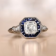 A stunning sapphire halo vintage engagement ring features a lively 1.01-carat Asscher cut diamond set in handcrafted platinum. Surrounded by a halo of sapphire, the center gem is GIA certified as J color and vvs2 clarity. A triple wire shank leads to accent stones on either side. ✦ DIAMOND SPECIFICATIONS: Diamond-Cut: Asscher Cut Diamond Clarity: VVS2 Diamond Color: J Color Diamond Weight 1.01ct ✦ ENGAGEMENT RING SPECIFICATIONS: Ring Material: Platinum Stones: Diamond, Sapphire ✦ WHAT COMES IN Y Gia Certified Art Deco Sapphire Ring For Formal Occasions, Gia Certified Art Deco Platinum Jewelry, Art Deco Gia Certified Collectible Rings, Collectible Art Deco Gia Certified Rings, Vintage Gia Certified Sapphire Ring For Formal Occasions, Gia Certified Art Deco Octagon Ring, Art Deco Sapphire Jewelry Gia Certified, Classic Octagon Sapphire Ring, Art Deco Platinum Octagon Ring