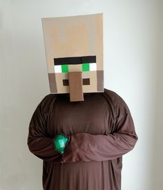 a man in a brown shirt is wearing a minecraft mask and has his hands on his hips