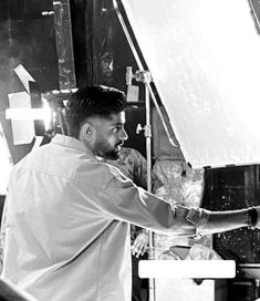 black and white photograph of a man in front of a large light fixture, working on something