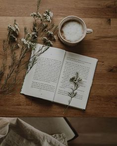 an open book sitting on top of a wooden table next to a cup of coffee