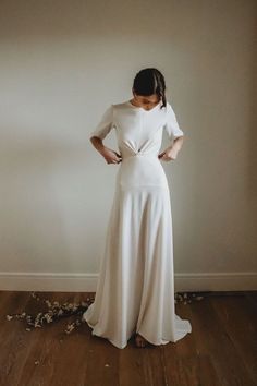 a woman standing in front of a wall wearing a long white dress with an open back