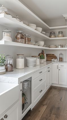 a white kitchen with open shelving and lots of dishes on the counter top,