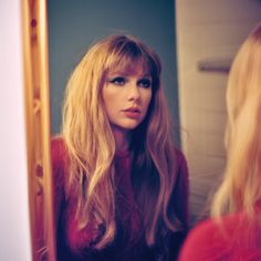 a woman with long blonde hair is looking in the mirror and she's wearing a red sweater