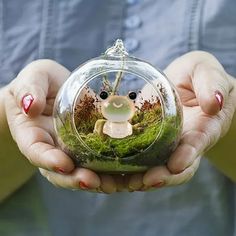 a person holding a glass ornament with a small animal in it's hands